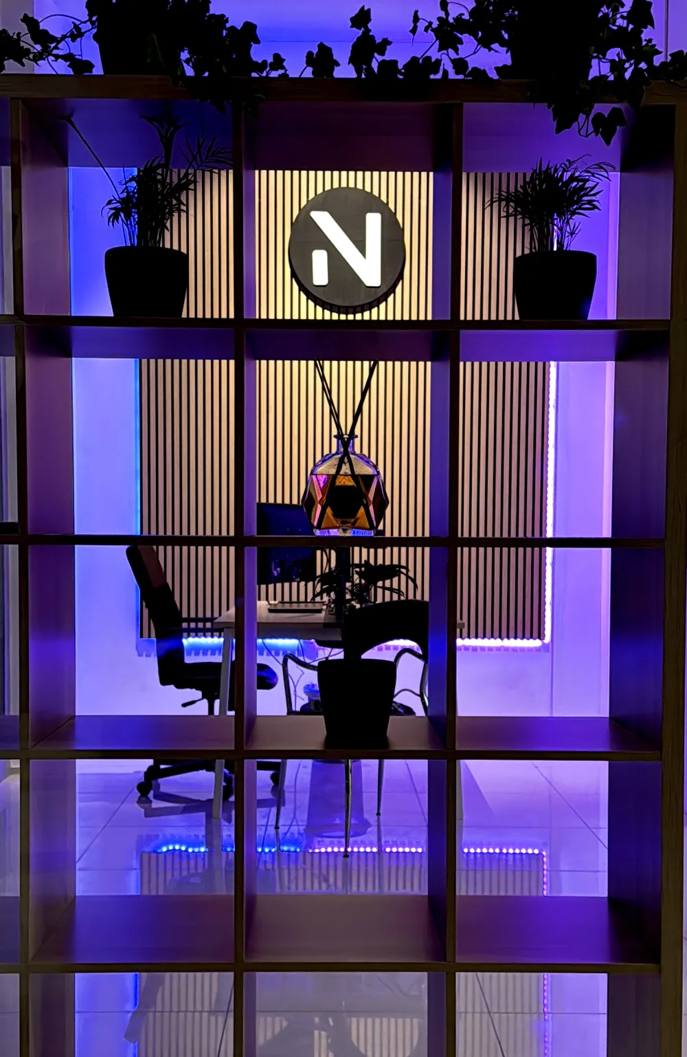 Il logo Neospot sulla parete in legno del nostro ufficio, tra piante e luci viola